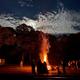 Nighttime bonfire scene with campers gathered and an RV visible at left — shows campground events/social atmosphere; image appears in the site’s social/background gallery. 