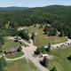 Clear high-resolution drone/aerial view showing the campground layout (roads, RVs, cabins, open grassy areas) and surrounding forest — excellent overall property overview; sourced from the site's drone images.