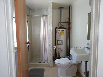 A bathroom with toilet, sink, water heater, and shower.