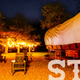 Nighttime scene of a wagon with string lights and seating around a campsite — attractive evening view highlighting ambiance and lighting on-site (present on site hero/stay imagery).