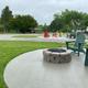 Concrete firepit pad with Adirondack chairs and nearby gravel pads / picnic tables — a communal campsite/amenity photo consistent with the campground's 'ways to stay' images on the property page.