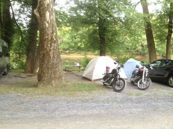 Tent campsite area with picnic table, trees and parked motorcycles — useful view of tent camping spaces and wooded surroundings shown on the property’s gallery.