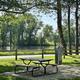 Riverside campsite view: picnic table, utility pedestal and fence with trees and water beyond — shows on-site riverfront pitches and setting (image hosted on property site ‘waterview’).