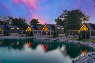 Evening exterior of multiple resort-style cabins reflected in the lake — clear, attractive shot of the cabins and waterfront referenced on the campground’s cabin booking page.