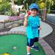 Child holding a mini‑golf ball on a putting green with landscaped surroundings — shows on‑site mini‑golf amenity and landscaped walkways. Present in the site’s activities images.