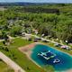 Aerial overview showing the campground layout, central swimming pond with inflatable waterpark, surrounding RV sites and tree line — clearly the property; image appears on the site’s gallery/background supporting overview context.