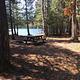 Campsite at Ninemile Campground. There is a picnic table in the shade of several trees and a lake in the background.