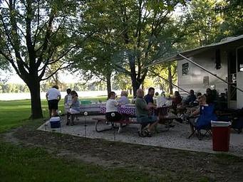 Large Group of people at campsite picnic tables.