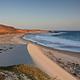 Sandy beach with ocean and small waves and steep coastal bluffs covered in dry grass. 