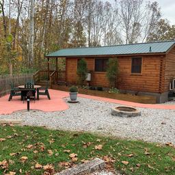 Photo of a cabin with a patio, fire pit and surrounding landscaping — clearly a campsite cabin on the property. It appears in the property's 'ways to stay' gallery on the KOA Brown County page.