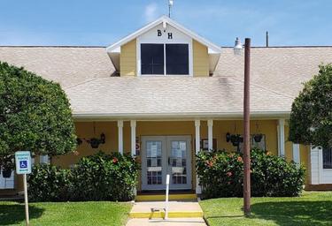 Front exterior of a yellow building labeled 'B H' (clubhouse/office) with landscaping — identifies an on-site facility visible in the resort’s photo gallery and page content.