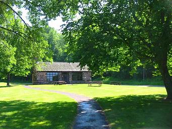 Distant view of the Black River Harbor Pavilion, sidewalk, and picnic tables outside on the lawn.