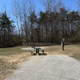 Open campsite with gravel pad, picnic table and utility pedestal framed by woods — useful depiction of a typical tent/RV site on the property (from Camping page imagery).