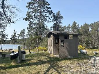 A photo of a vault toilet and trash receptacle at Wagner Lake (MI)