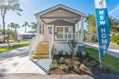 Exterior photo of a model/new home on a landscaped pad with a ‘New Homes’ banner — relevant to the property’s manufactured-home community and shown on the site as onsite housing.