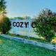 Alternate horizontal view of the fenced entrance sign with landscaping and sunlight — useful as a welcoming/hero image for the property gallery.