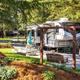 Clear photo of an RV site with a fifth-wheel, paved pad, picnic area and surrounding trees — labeled on the page as a 'ways to stay' campground photo, showing on-site RV accommodations.