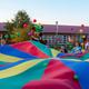 Wide, colorful photograph of a large group parachute activity on the campground grounds; shows cabins and open lawn in background—good overall view of onsite family activities and layout (used as social header on the property site).