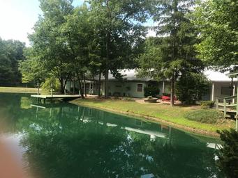 Exterior view of the main house/building along the pond with dock and trees — useful for illustrating the facility and waterfront setting (present on the site as cover image).