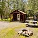 Cozy cabin beside picnic tables and a fire pit in the woods.