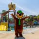 Wide view of the pool and water-play complex with slides and mascot in the foreground — strong depiction of the park’s aquatic facilities and family amenities.