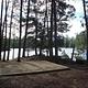 Square tent pad surrounded by trees and a scenic lake.