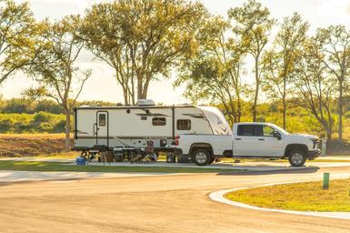 Ground-level photo of an RV and tow vehicle parked on a concrete pad beside landscaping — shows typical guest site setup and amenities.