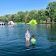 Wide waterfront view showing the campground's swim lake, inflatable water park structures and shoreline with trees — clearly shows a primary on-site recreational amenity (from the Lake Park page).