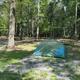 Clear photo of a tent pitched in a wooded campsite showing gravel pad, picnic table and surrounding trees — good depiction of tent camping at Camp Hebron (from the campground lodging page).
