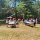 Open grassy area with people, picnic tables and a cabin/structure in the background — illustrates common area/amenity space and campsite atmosphere on the property (from Activities page).