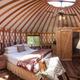 Pacific‑style yurt interior showing bed, rustic finishes and windows — directly matches the site’s yurt accommodations and glamping offering.