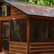 Exterior photo of a screened wooden cabin among trees (page header for Cabins) — clearly shows the property’s cabin accommodations and wooded setting.