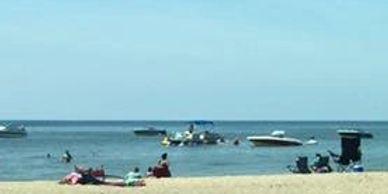 Boats anchored near a beach with people enjoying a sunny day.
