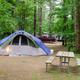 Tent campsite with picnic table and surrounding trees — representative photo of wooded tent sites on the property; sourced from the campground 'ways to stay' images.