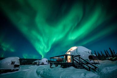 Striking nighttime scene of igloos with strong aurora overhead; useful for marketing the on-site experience and atmosphere (page: Accommodations).