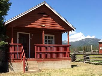 Paddy Flat Guard Station East - front of rustic cabin showing porch and stairs with blue skies and mountains beyond