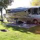 Close view of an RV on a concrete patio with awning, picnic table and grassy site area — clearly depicts full-hookup RV campsite amenities available at the KOA.