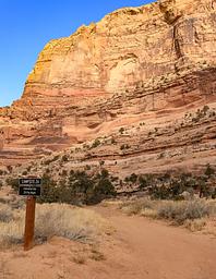 A dirt road with a sign for Campsite 26 leads towards the base of an orange sandstone cliff