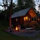 Cabins at dusk with lit porch, picnic table and fire pit — good representation of the park’s cabin lodging and campsite ambiance (used on site slide for cabins).