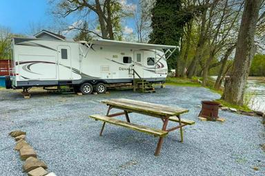 RV/trailer seasonal site with gravel pad, picnic table and fire ring — useful depiction of a typical seasonal/RV campsite on the property (matches ‘seasonal sites’ page context).