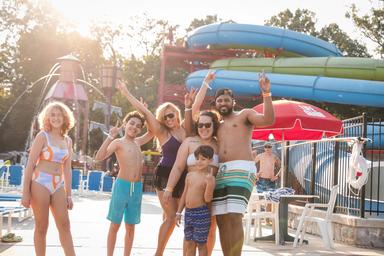 Family group posing at the pool with water slides visible behind them — shows scale of pool area and guest experience at the resort’s aquatic facilities.