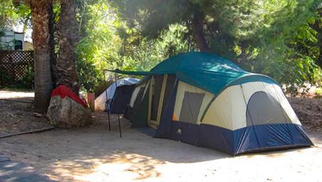 Tent camping site image showing a multi-room tent beneath trees and campground surroundings — useful to show non-RV camping options.