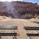 Group campsite, picnic tables, fire pit, and grill with sun setting behind cliffs in background