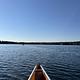 The front of a canoe surrounded by a blue lake with another canoe in the distance.