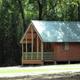 Another high-quality exterior cabin shot (cabin with green roof and trees) that shows setting and scale of lodging; sourced from the accommodations page background.