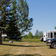 Wide panoramic shot of multiple RVs parked on grassy sites with shade trees and campsite amenities — useful overall view of the campground layout (homepage slide showing campground grounds).