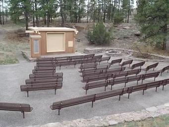 Amphitheater with brown benches and a tan building surrounded by pine trees