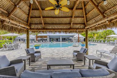 Resort pool area seen from under a tiki-style palapa with loungers and pool beyond — from the gallery demonstrating the main guest leisure facility.