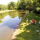 Aerial/overhead view of the campground pond with people along the shoreline — provides an overview of the water feature and adjacent grounds.