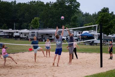 Sand volleyball court with RVs and campsites visible in the background — shows recreational facilities and adjacent camping spaces on-site (used on site background content).